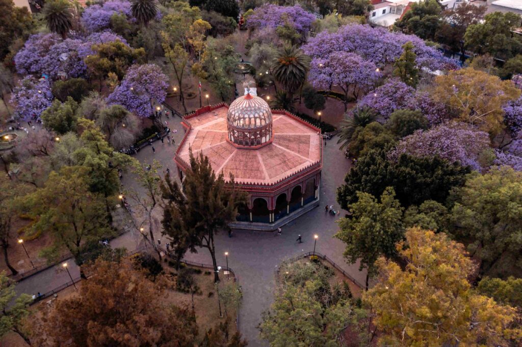 Aerial view of the historic Kiosco Morisco pavilion surrounded by blooming purple jacaranda trees in a public park in Santa María la Ribera, Mexico City.