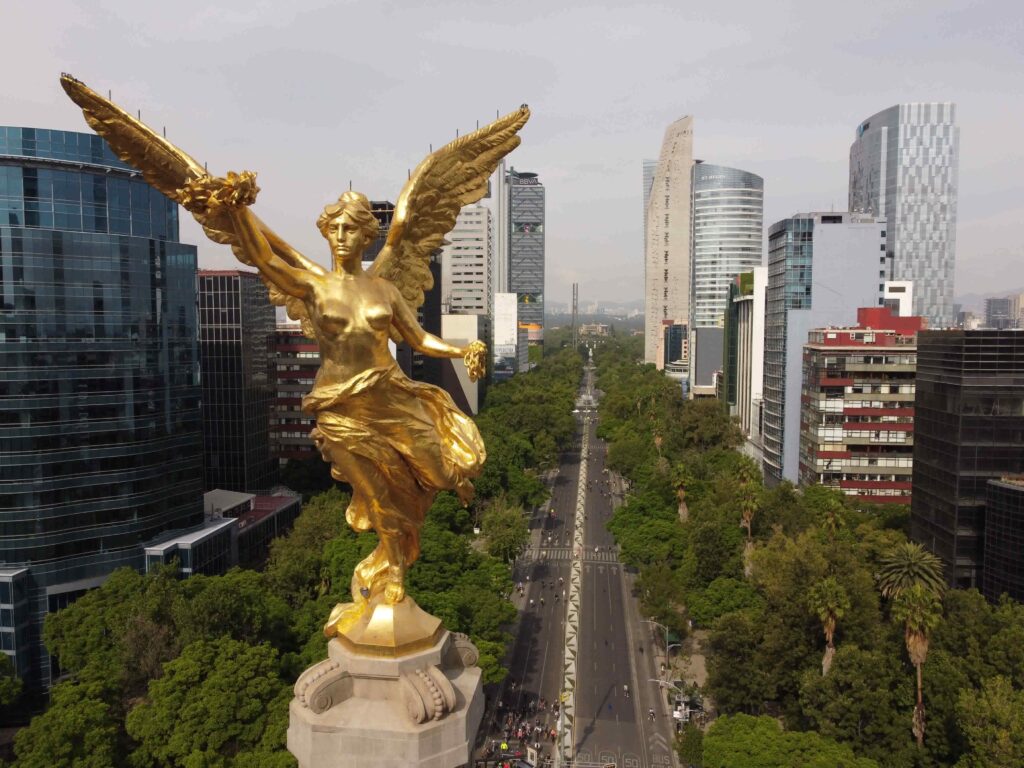 Aerial view of the golden Angel of Independence statue overlooking Paseo de la Reforma avenue with skyscrapers in Mexico City.